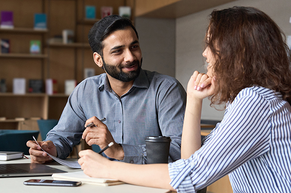 Couple sitting at a table, reviewing paperwork and smiling at each other.